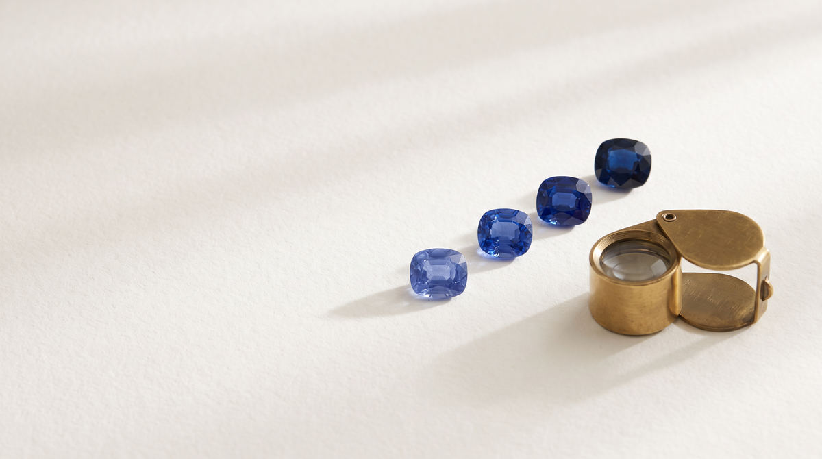 Four blue sapphires in different tones beside a brass loupe
