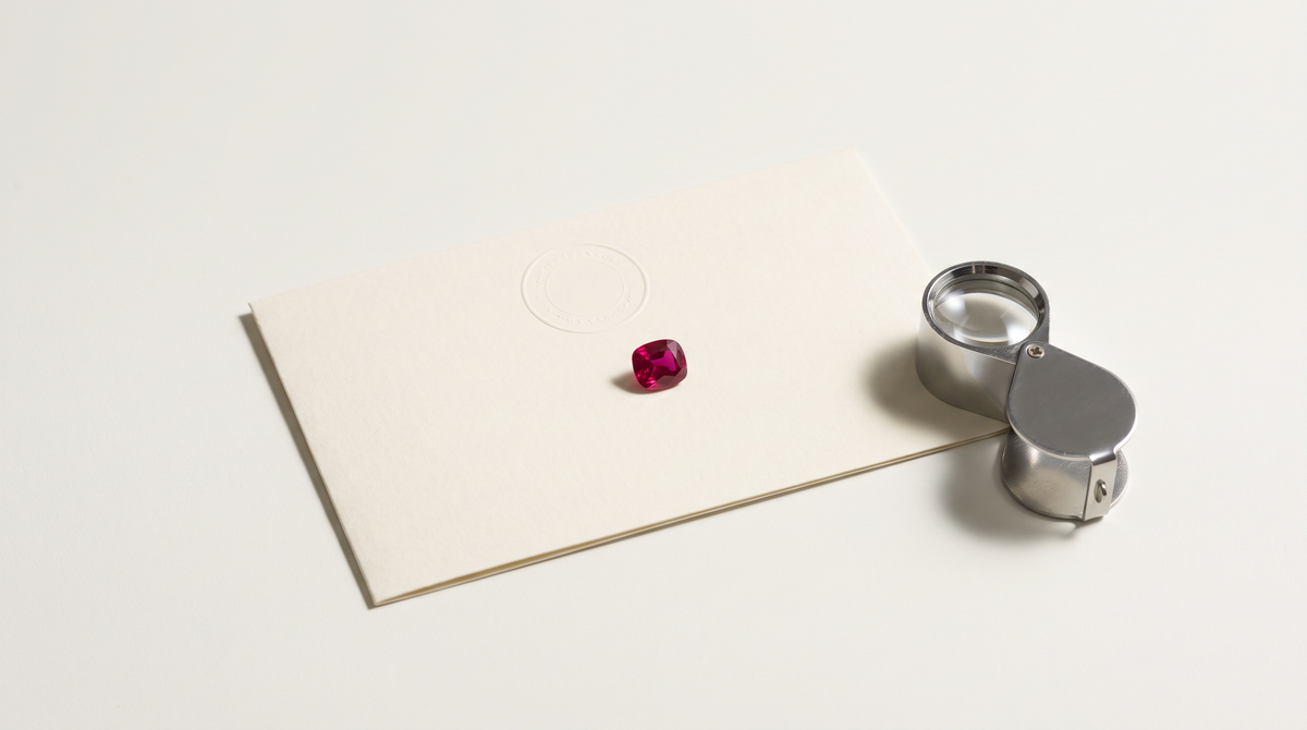A small ruby on a blank laboratory report card beside a loupe